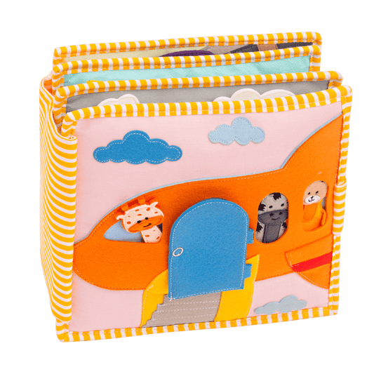 Livre textile Jolly Designs Globetrotter ouvert sur une activité en feutrine avec porte bleue, ciel nuageux et personnages en tissu.