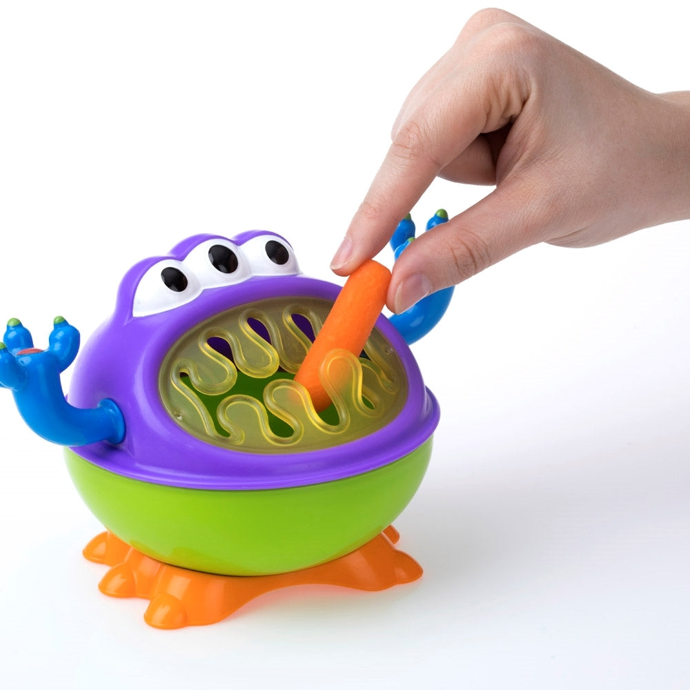 Main tenant une carotte dans l’ouverture souple du porte-collation 3D Monster Nûby multicolore.