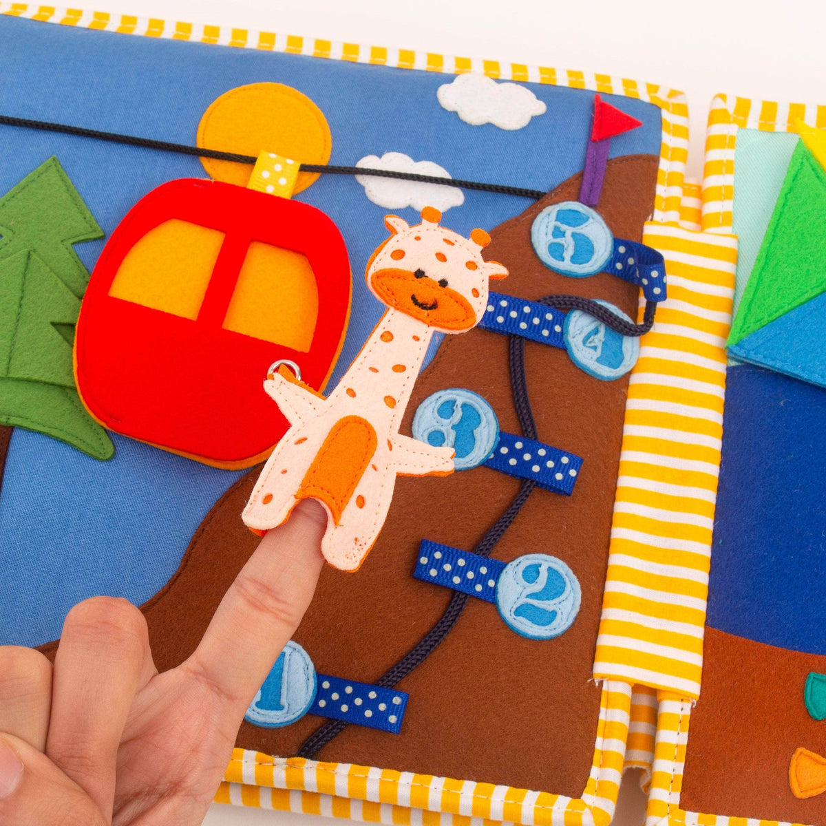 Page de transport du Quiet Book Globetrotter Jolly Designs avec cabine rouge mobile, girafe et éléments de motricité en feutrine.